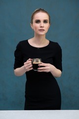 Studio portrait concept of a beautiful fashionable blonde girl standing in a business dress on a blue background drinking coffee.