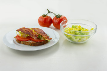 BLT sandwich on a white plate with lettuce and tomatoes on the side with a white background.