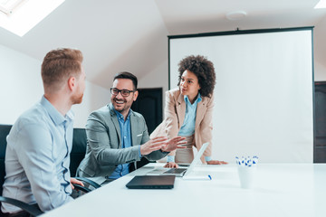 Positive millenial business team discussing project in meeting room.