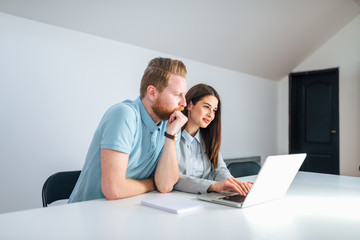 Two millenial entrepreneurs looking at laptop screen in a bright meeting room.