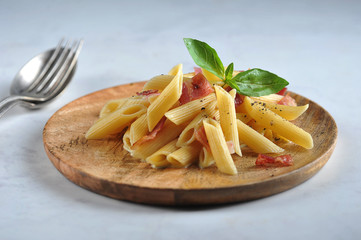 Pasta carbonara on a wooden plate. Pasta is decorated with green basil. Light background. Close-up.