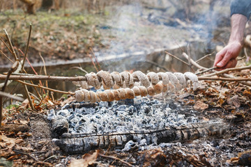 The cook prepares the dough on skewers on the fire in the spring forest