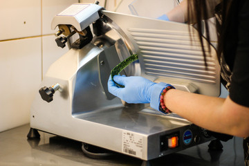 The girl's chef is preparing green crepe rolls with basil cheese. Slicing cheese on a machine slicer