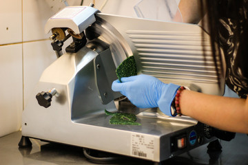 The girl's chef is preparing green crepe rolls with basil cheese. Slicing cheese on a machine slicer