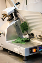 The girl's chef is preparing green crepe rolls with basil cheese. Slicing cheese on a machine slicer