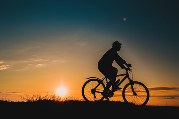 Fototapeta premium Silhouette of a male mountainbiker at sunset in the mountains