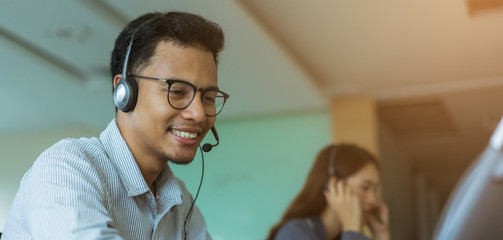 close up asian man call center agent wear headset device and smiling working in operation room with service-mind at  desktop table , telemarketing and help desk concept - obrazy, fototapety, plakaty