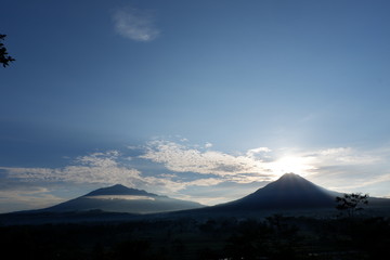 the view of the sun rises from behind the mountain, with a blue cloud background