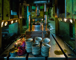 dirty used low tech stamping press producing round aliminium parts in dark environment