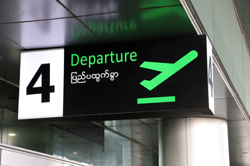 Fototapeta premium Departure sign in english and Myanmar language with symbol of the plane take off in green on black color at the gate number 4.