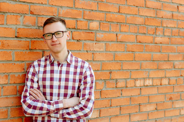 Fototapeta na wymiar Portrait of a guy in a shirt and glasses against a brick wall