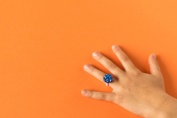 Funny ring on a little girl's hand. Isolated on orange background.