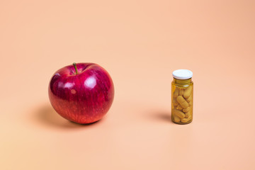Pink pills in the glass bottle and apple on a orange background