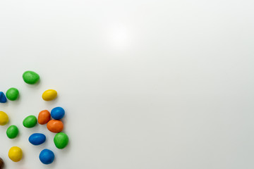 Multicolored candies (dragees) in the glaze scattered on a white background. Place for text