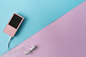 Top view. Portable music pink player and earphones on a purple and blue background, that is divided diagonally. Place for text