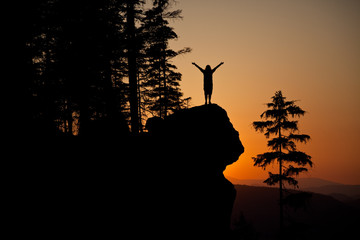 Silhoutte of a young woman posing on a rocky cliff against a colorful sunset, In Czechia, Europe