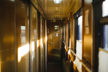 Empty sunlit corridor of passenger train in warn colors. Train car interior. Concept of traveling and journey.