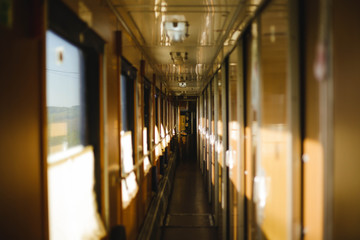 Long empty sunlit corridor of passenger train in warn colors. Train car interior. Concept of traveling and journey.