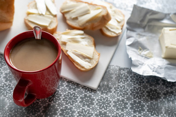 Morning red cup of coffee with milk and bread with butter ( sandwich) on the white board  on the table in kitchen. Tasty breakfast 