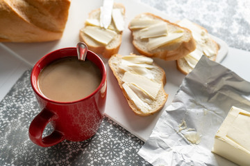 Red cup of coffee and bread with butter ( sandwich ) on the white board  on the table in kitchen. Tasty breakfast 
