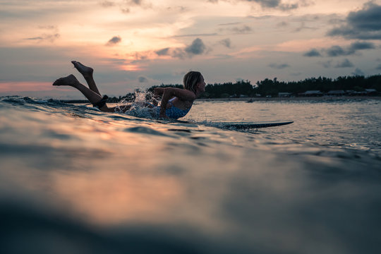 Young woman surfing waves in the ocean at sunset