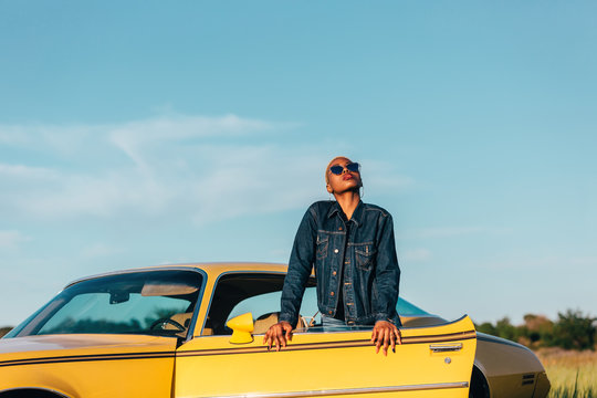 Beautiful african woman leaning to a classic yellow car