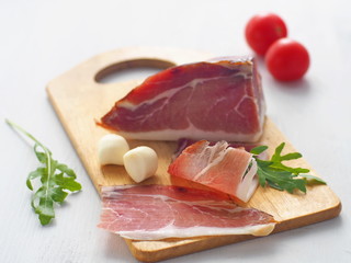 Fresh meat upon white table. Prosciutto, prsut, or Spanish jamon with cherry tomatoes, fresh arugula and mozzarella. Selective focus.