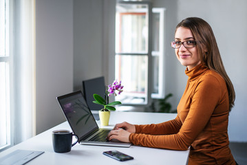 Pretty young smart looking woman with glasses working standing at the desk