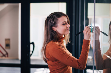 Young girl writing sticky notes on the glass door as reminder or brainstorming