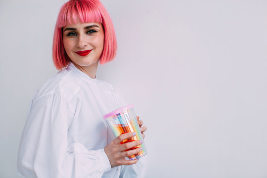 Smiling stylish girl with pink hair hold holographic cup of beverage by white background