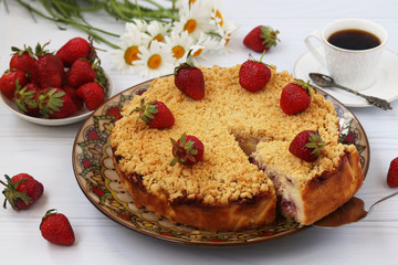 Curd cake with strawberries with a cut out piece of cake is located on a white background surrounded by a cup of coffee