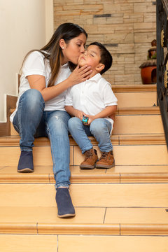 Young mom giving a kiss on the cheek to her 4 year old son sitting on the steps of his house