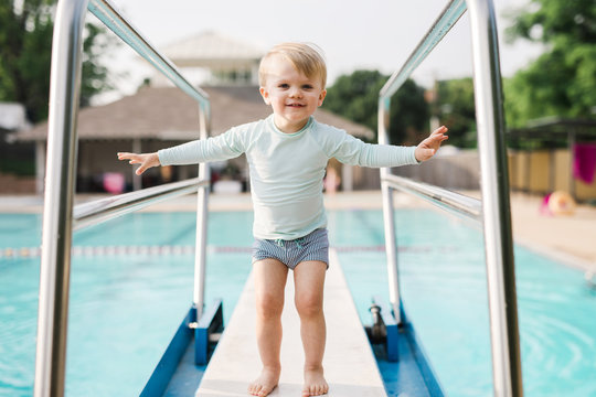 little toddler happy to stand on a big diving board at the pool
