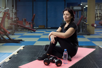 Senior woman in the gym sitting on a pink yoga mat. close-up. copy space.