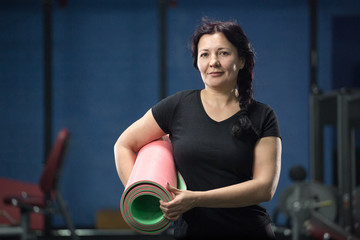 Senior woman at the gym holding a pink yoga mat. close-up. copy space.