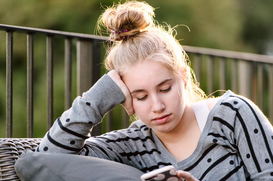 Close up of a teenage girl sitting outside using her phone at sunset
