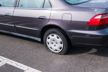 Car with a flat cracked tire on an asphalt parking lot.