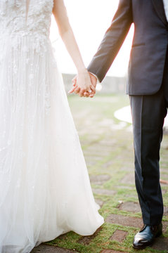 A bride & groom hold hands as golden sunset light pours through