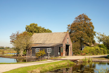 Fototapeta na wymiar Old crooked barn surrounded by water in Dutch landscape.