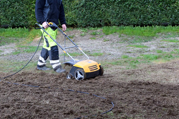A man cuts moss in the garden with an aerator. Concept: Lawn aeration before planting lawn grass. Garden work with tools.