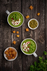 Broccoli cream soup, vertical, copy space, top view. Vegetable green puree in two large white cup. Diet vegan soup of broccoli, zucchini, green peas on dark wooden background