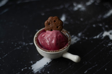 Berries ice cream in a white bowl with chocolate cookies   on dark background. Summer vibes