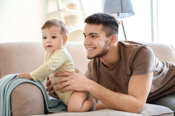 Young dad with his little son on sofa at home