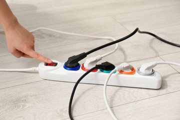 Woman pressing power button of extension cord on floor, closeup. Electrician's professional equipment