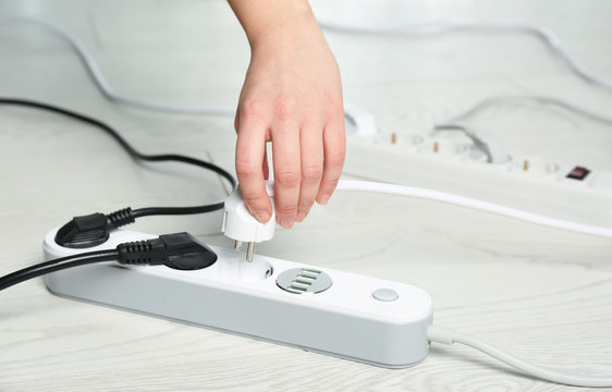 Woman inserting power plug into extension cord on floor, closeup with space for text. Electrician's professional equipment