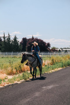 cowgirl rides roan horse down country road