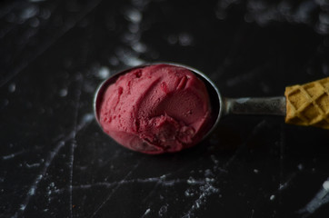 Homemade strawberry ice cream with one large scoop on black background