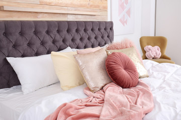 Comfort bed with pillows at wooden wall in modern room interior