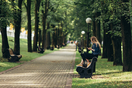 lonely woman waiting at park, entertaining with her smartphone.