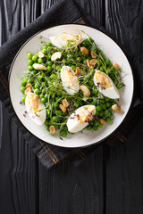 Green spring salad made from peas, micro greens, nuts and eggs close-up on a plate. Vertical top view
